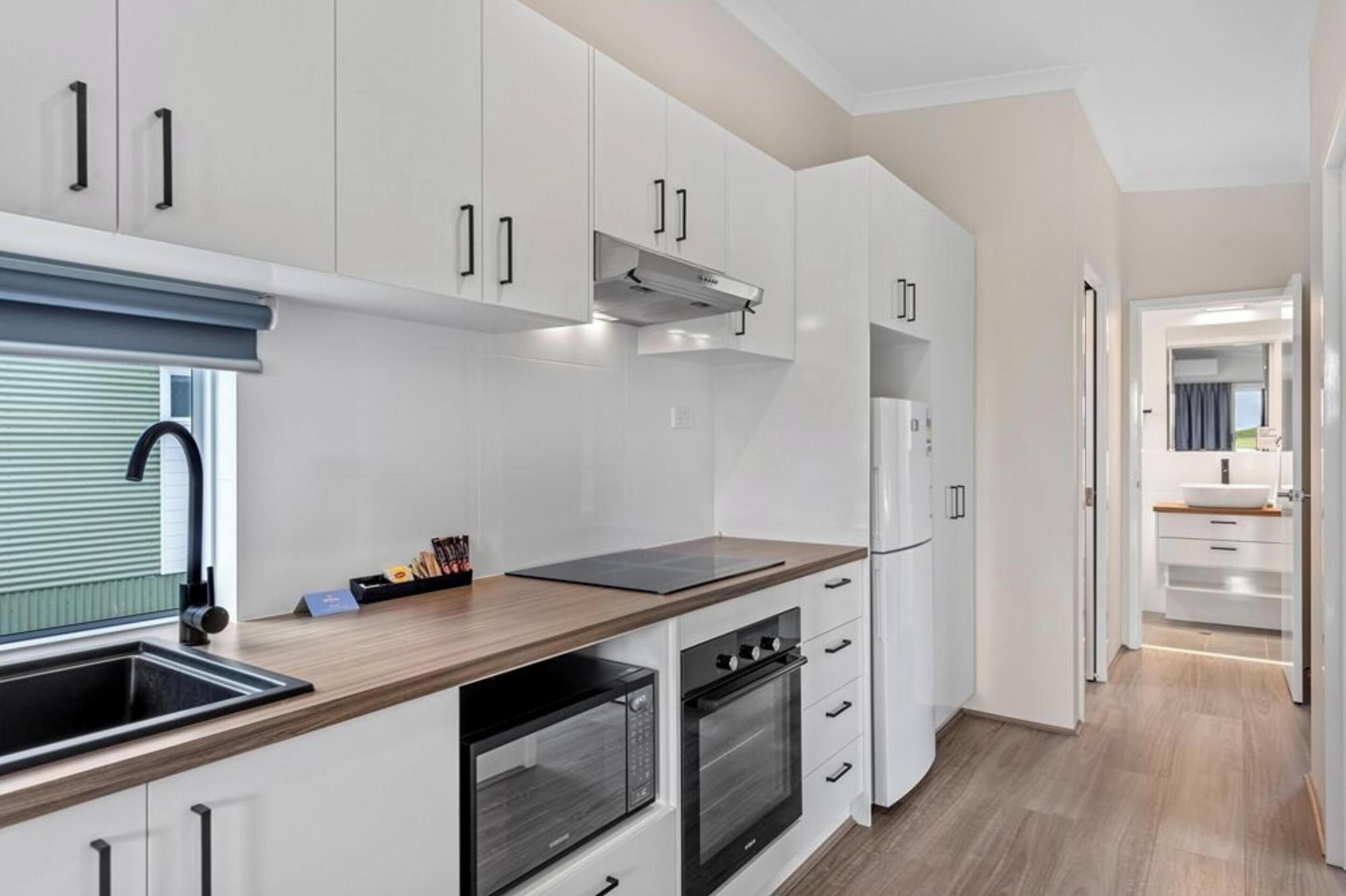 Una cocina moderna con armarios blancos, encimera de madera, horno empotrado y campana extractora de acero inoxidable.