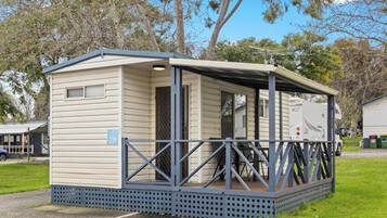A small, single-story mobile home with a covered porch and a fenced deck area.