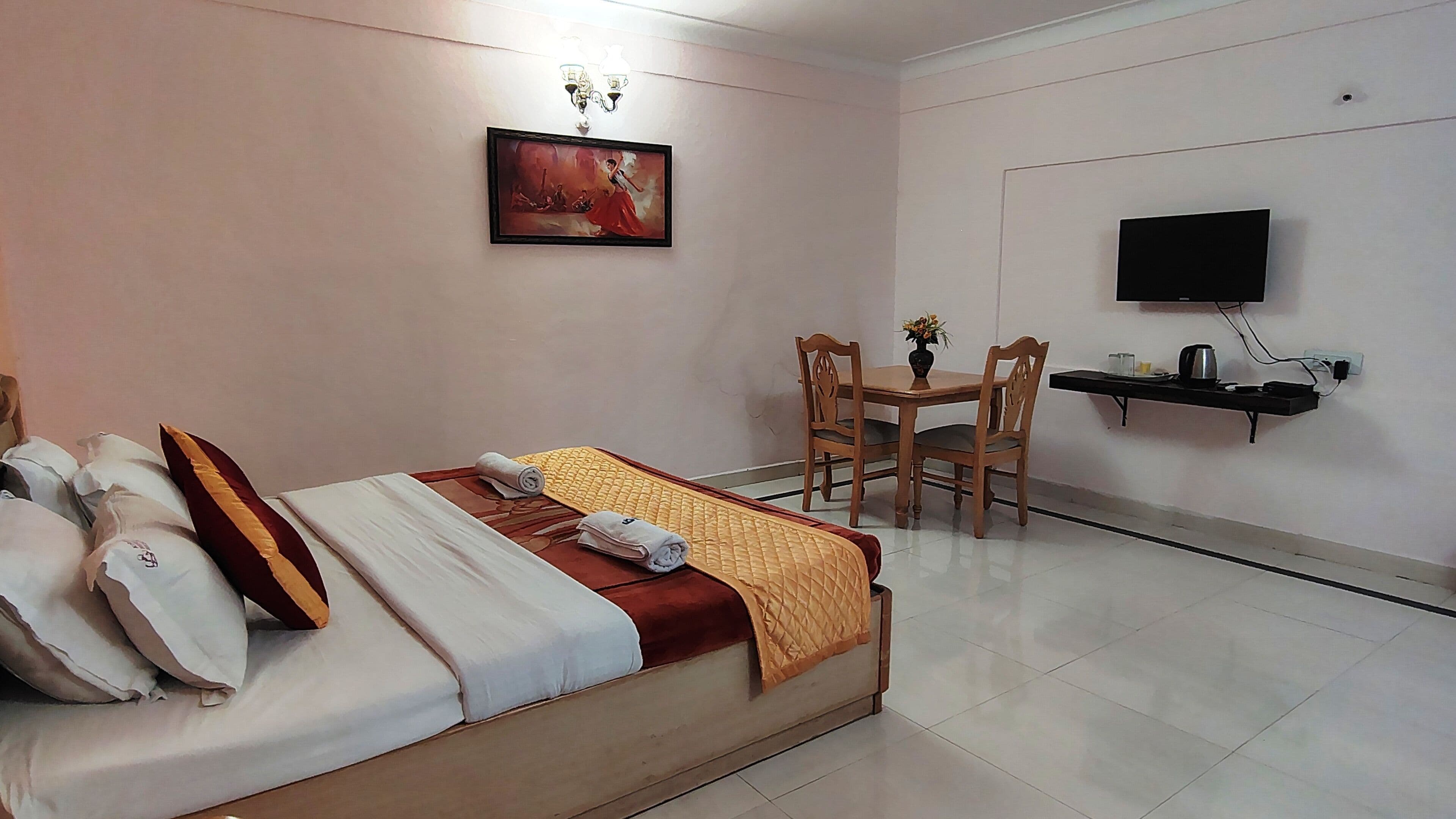 Quarto de hotel com cama, escrivaninha, cadeira, televisão e um quadro na parede.