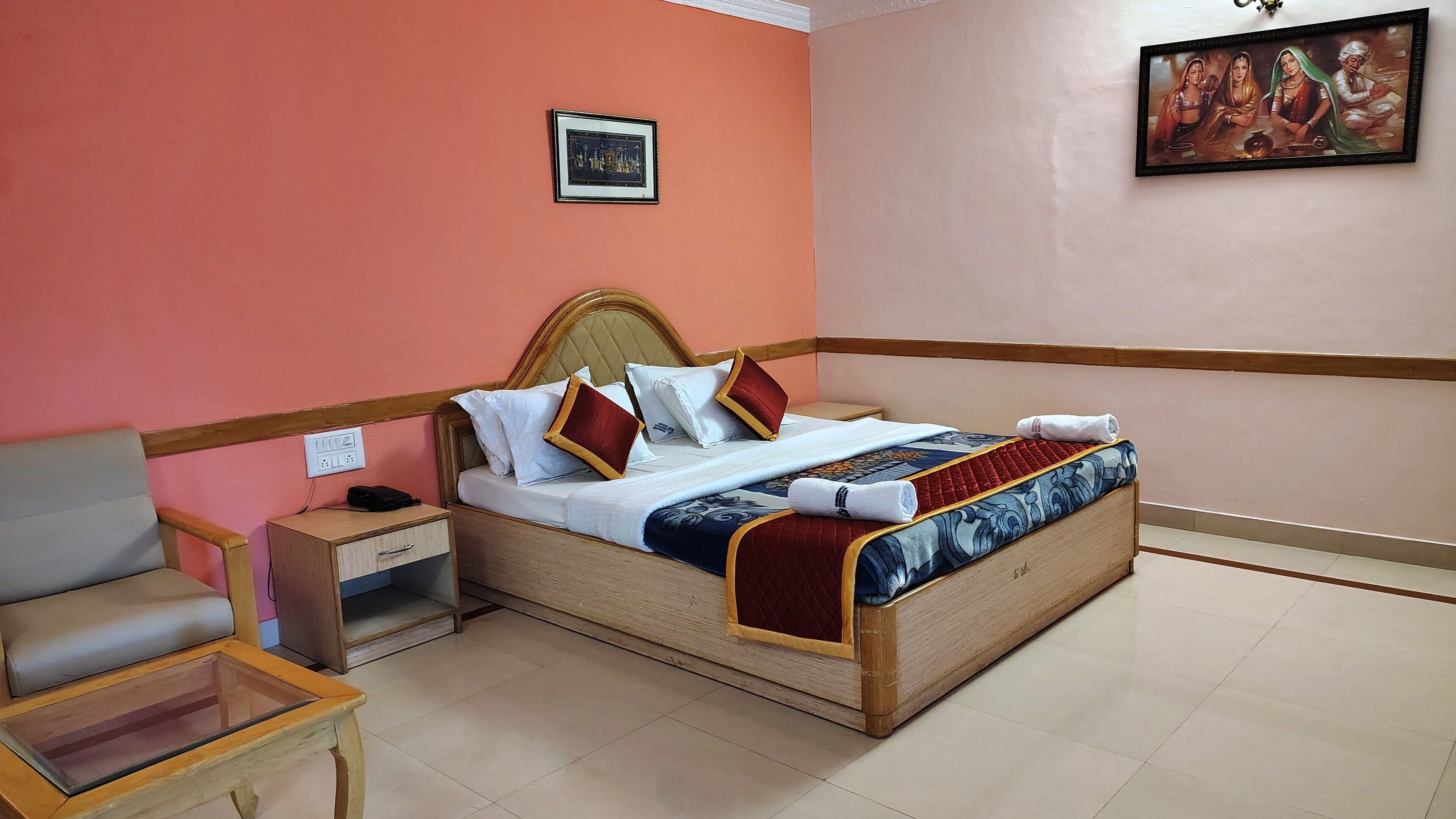 A neatly arranged hotel room with a bed, bedside table, chair, and a small table with a glass top.