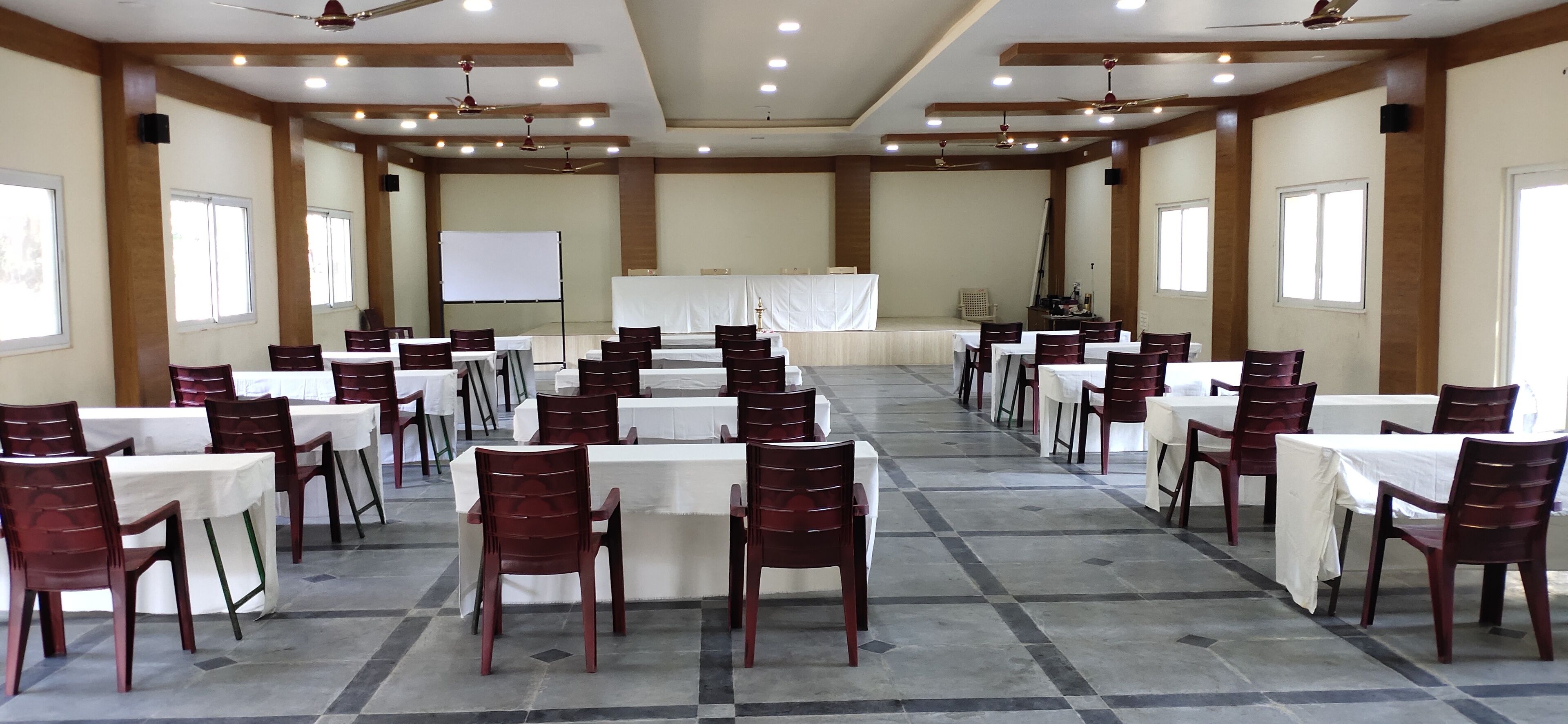 A conference room with multiple tables and chairs, a whiteboard, and a stage.