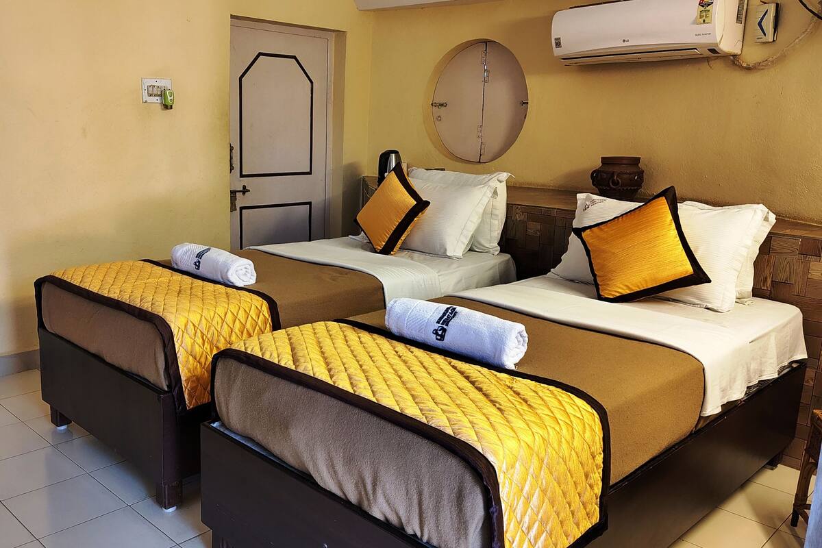 A hotel room with two beds, each with a yellow quilted bedspread and white linens. There is a door with a handle, a wall-mounted air conditioner, and a small table with a lamp.