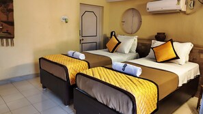 Habitación de hotel con dos camas, cada una con cubrecama acolchado amarillo y ropa de cama blanca. Se observa una puerta con manija, un aire acondicionado instalado en la pared y una mesita de noche con una lámpara.