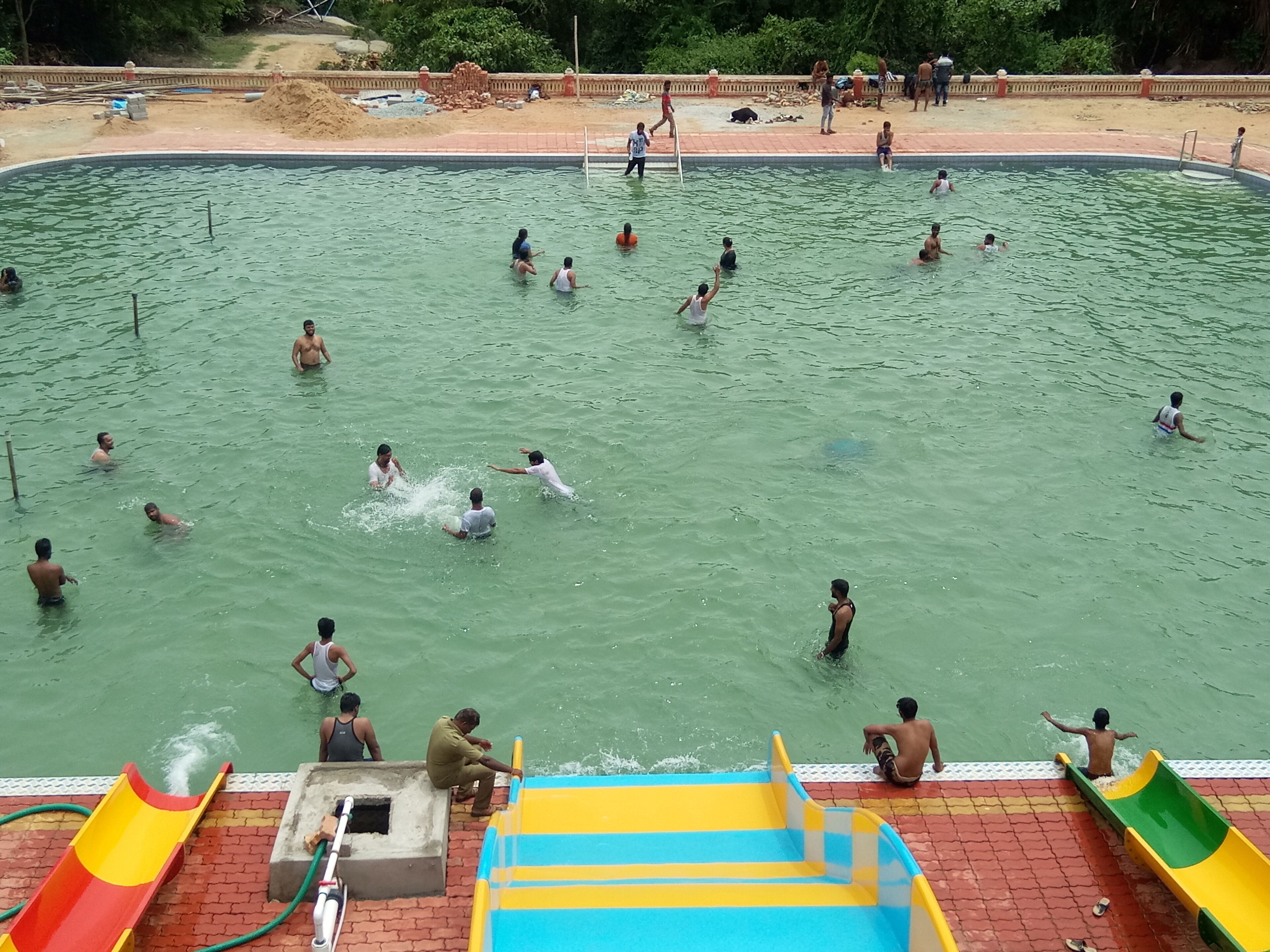 A swimming pool with multiple people in the water, surrounded by a brick deck and a slide.