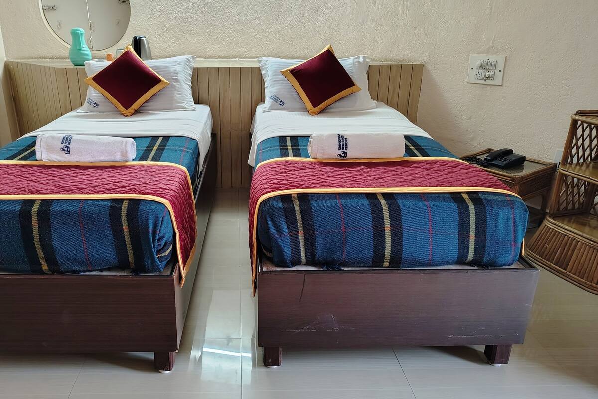 A room with two single beds, each with a plaid blanket and a red quilted top. There is a wooden headboard, a bedside table with a phone, and a mirror on the wall.