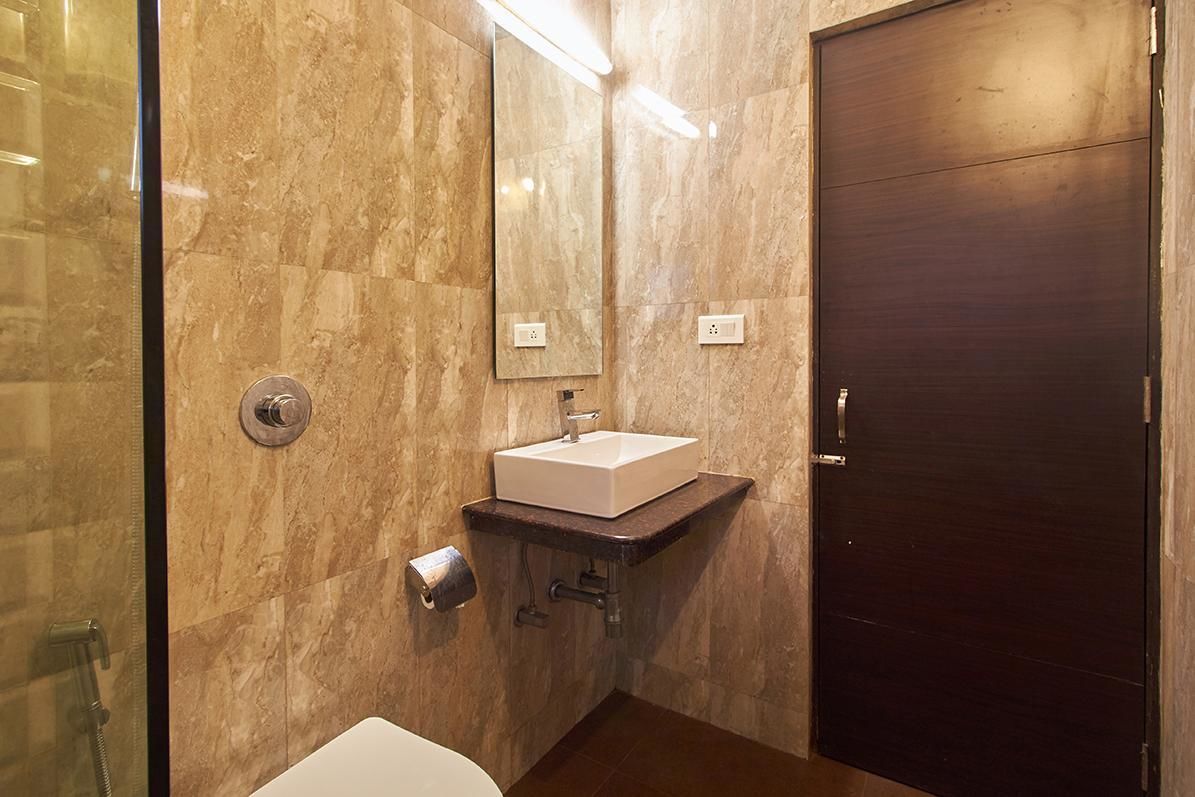 A modern bathroom with a marble wall, a white sink, a mirror, and a dark wooden door.