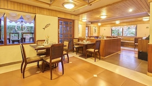 A restaurant with wooden interiors, a dining area with tables and chairs, and a view through large windows. - SinQ Beach Resort (Calangute)