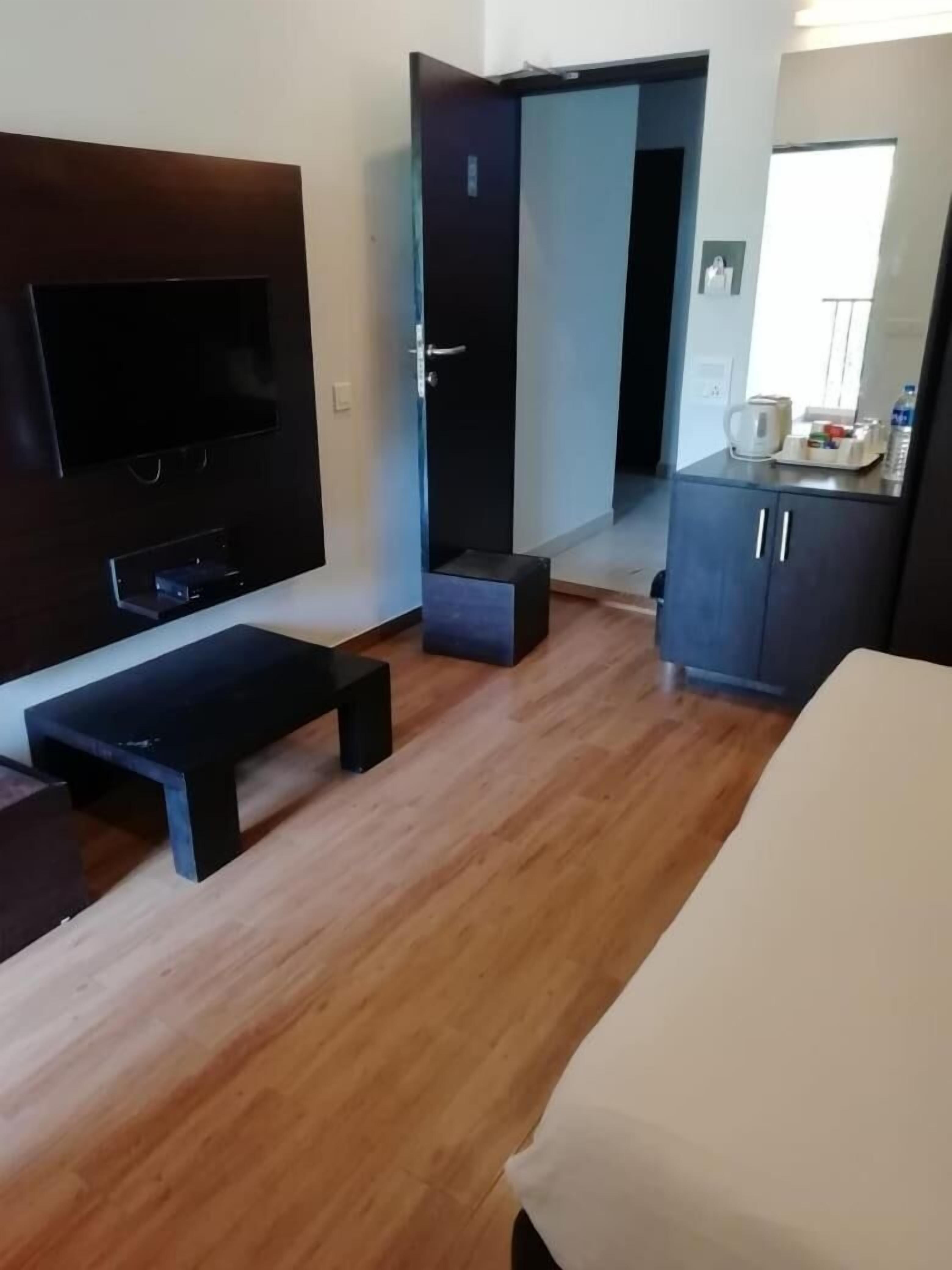 A modern hotel room with a wooden floor, a flat-screen TV, a bed, a small table, and a wardrobe.