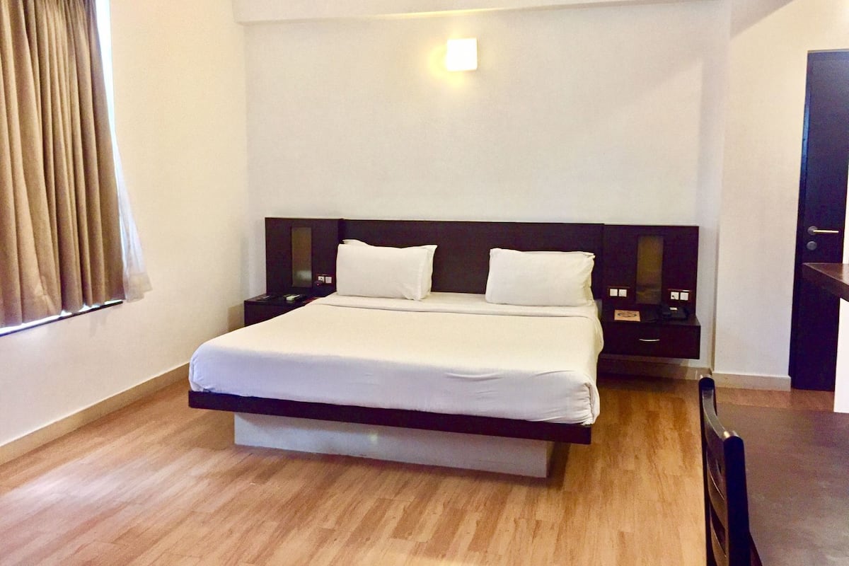 A hotel room with a bed, bedside tables, a nightstand, a desk, and a chair.
