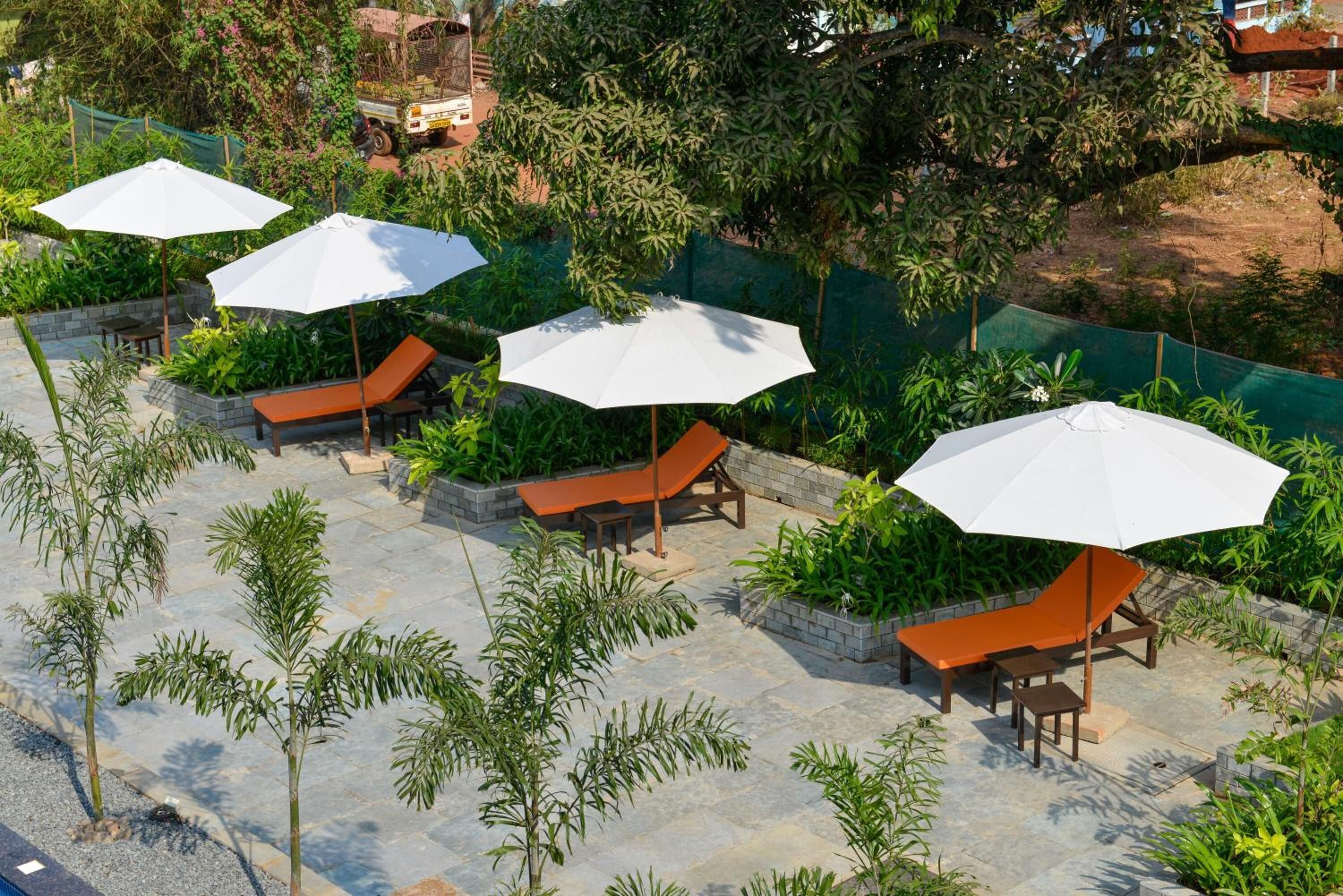 A rooftop garden with outdoor seating areas, including lounge chairs and umbrellas, surrounded by greenery and trees.
