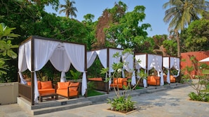 A row of outdoor seating areas with white canopies and orange cushions, surrounded by lush greenery. - SinQ Beach Resort (Calangute)