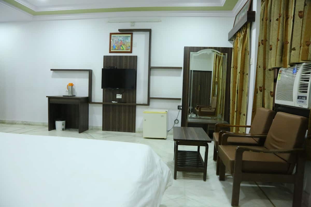 A hotel room with a bed, a desk, a chair, a television, a mini-fridge, and a mirror.
