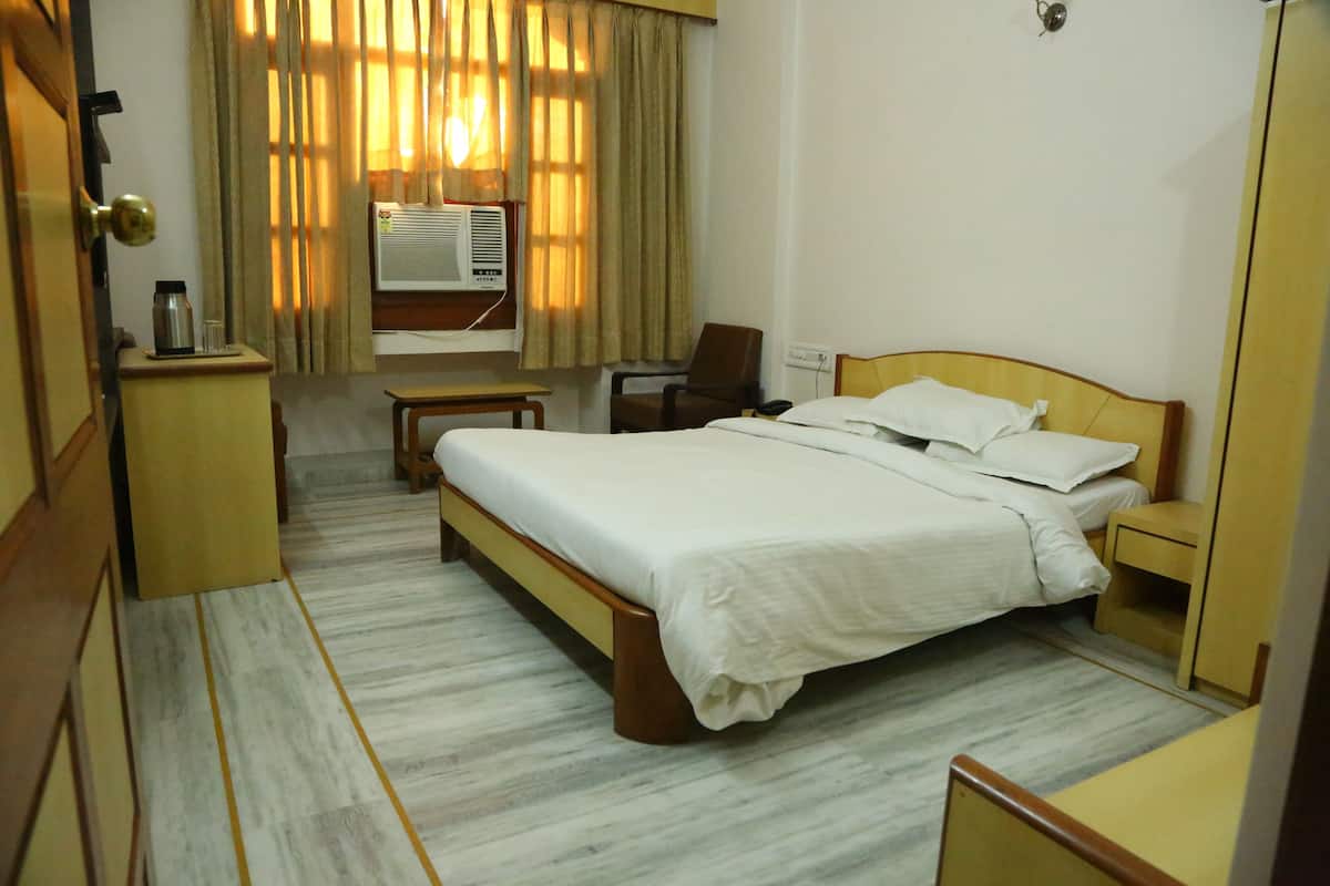 A hotel room with a bed, bedside table, chair, and an air conditioning unit.
