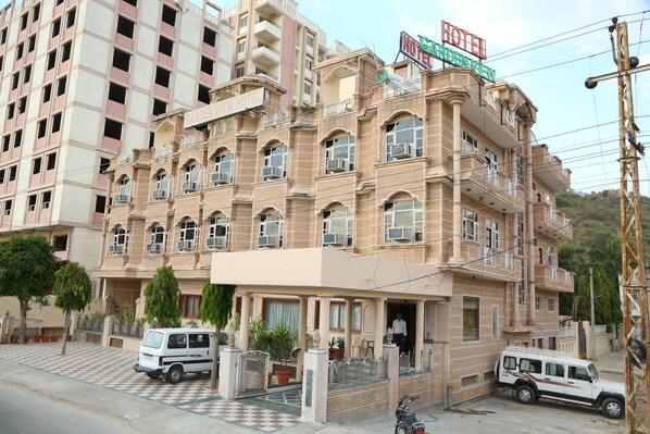 A multi-story hotel with a garden view sign, balconies, and a checkered pavement in front.
