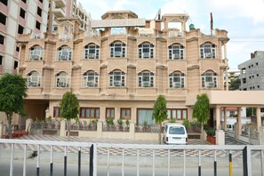 A multi-story hotel with a checkered pavement in front, air conditioning units on the facade, and a white van parked in front.