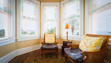 A corner room with a wooden chair and a sofa, both with floral cushions, a small table with a lamp, and a patterned rug.