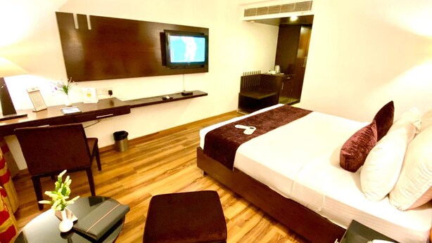 A hotel room with a bed, a desk, a chair, a TV mounted on the wall, and a bedside table with a phone. - GIS Select Banjara  Hills (Hyderabad)