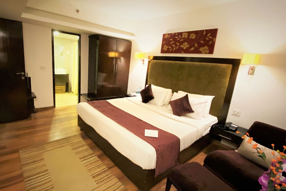 Habitación de hotel con una cama grande, una mesita de noche, una silla y una puerta que da a un baño.
