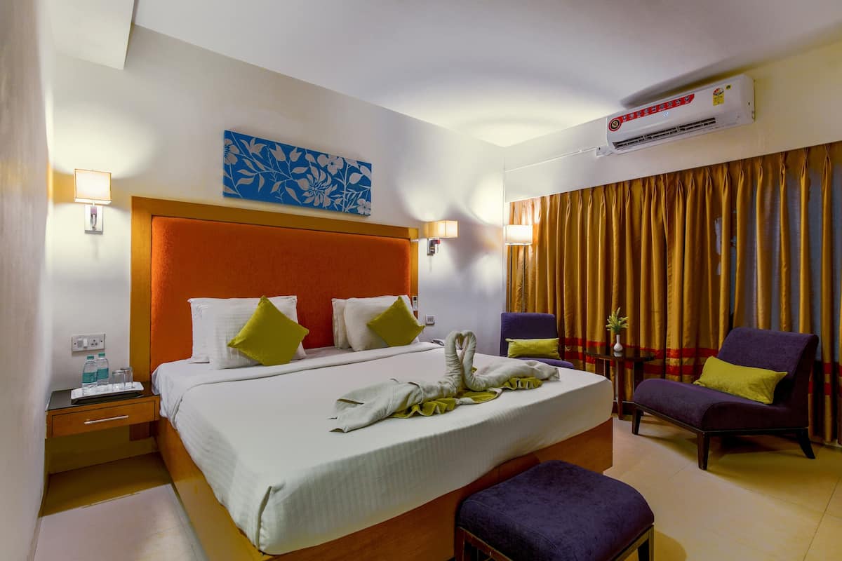 Habitación de hotel con una cama grande, una mesita de noche, una silla, aire acondicionado y una ventana con cortinas.