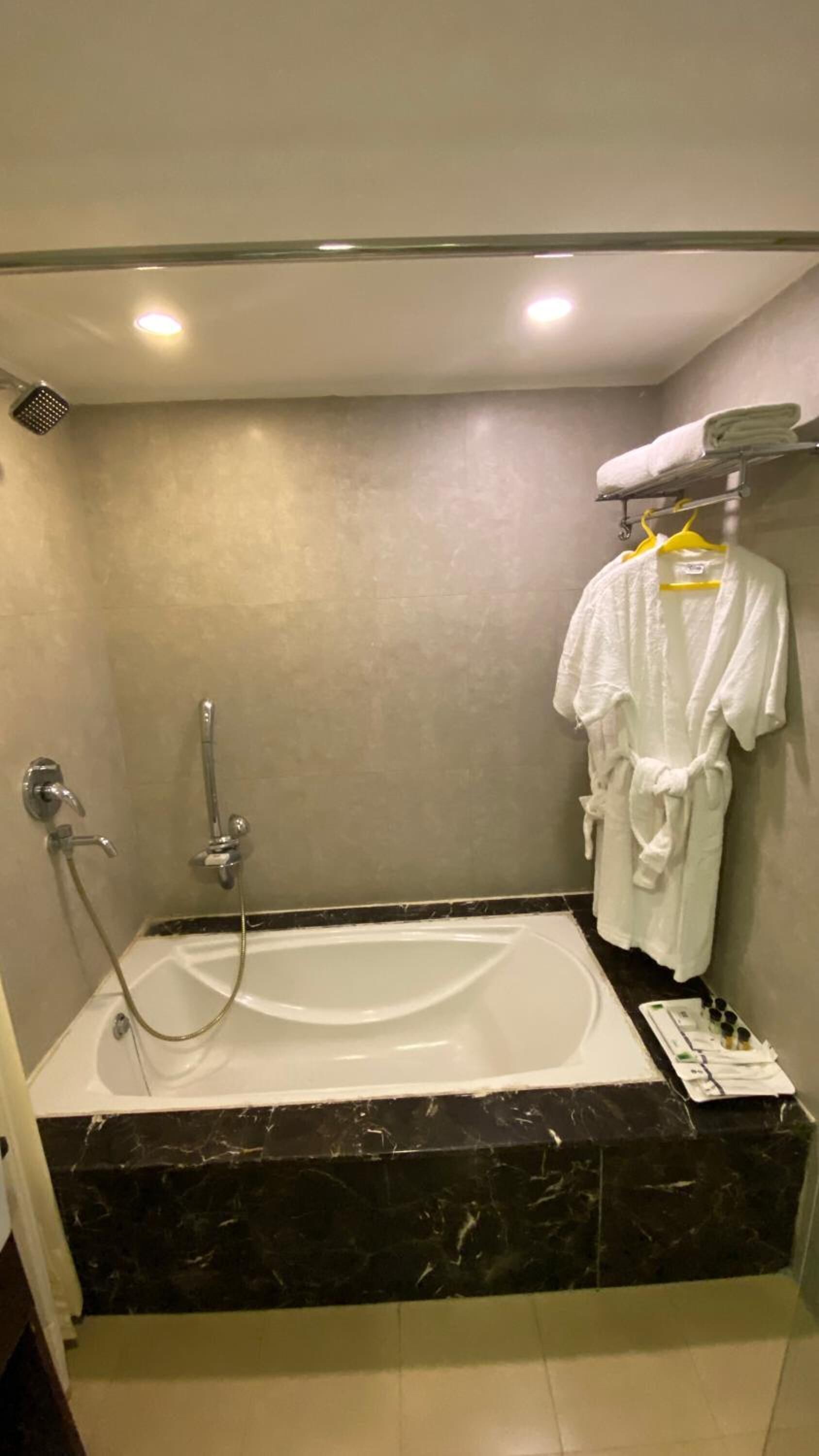 A bathroom with a bathtub, a shower, a towel rack with a white towel, and a bottle of shampoo on the counter.