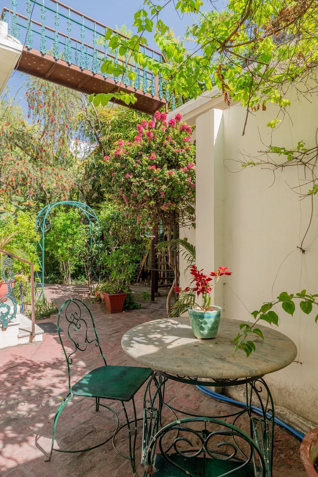 A patio with a round table and chairs, surrounded by potted plants and a metal trellis.