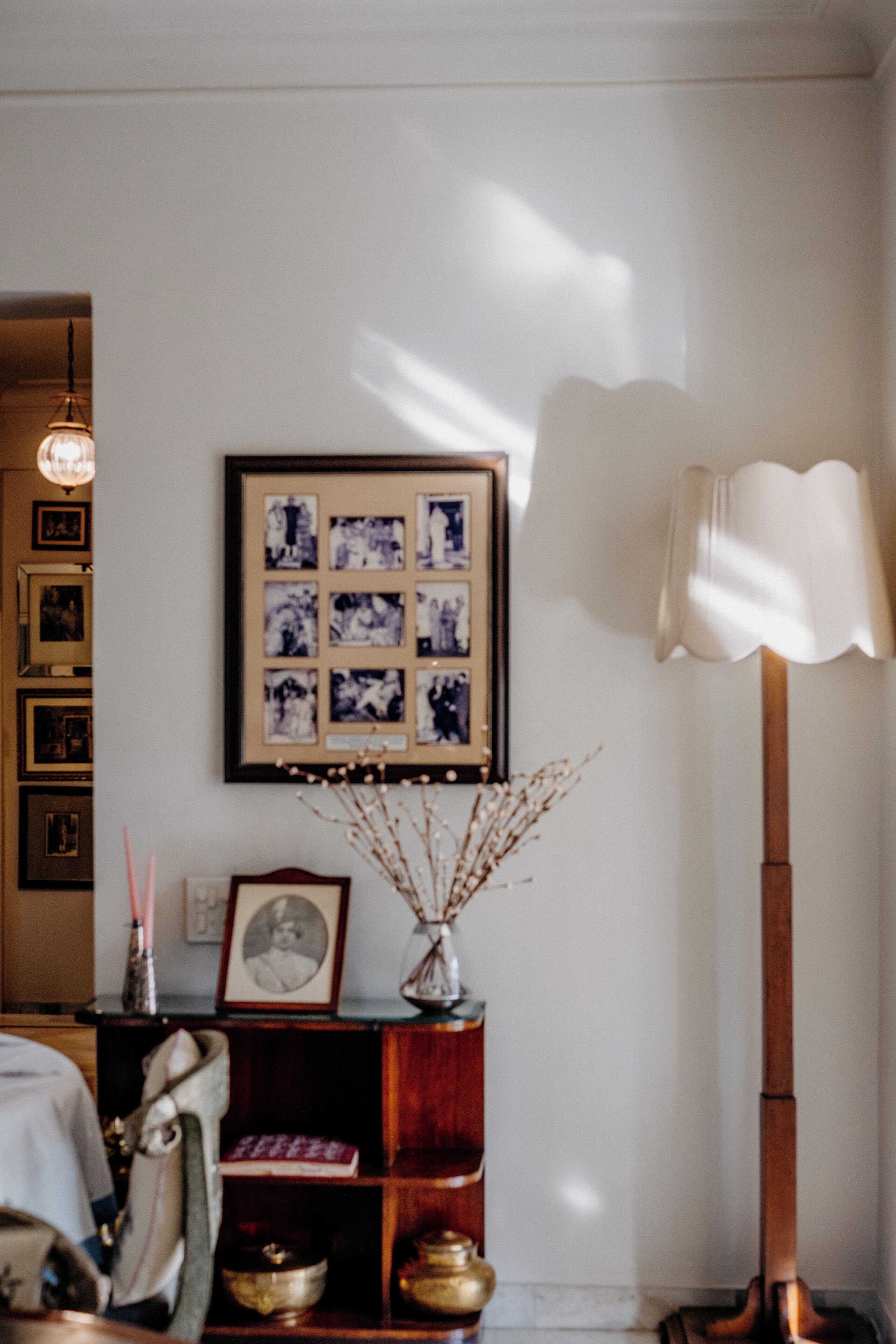 Una habitación con una composición de fotos enmarcadas, una lámpara y una repisa con objetos decorativos.