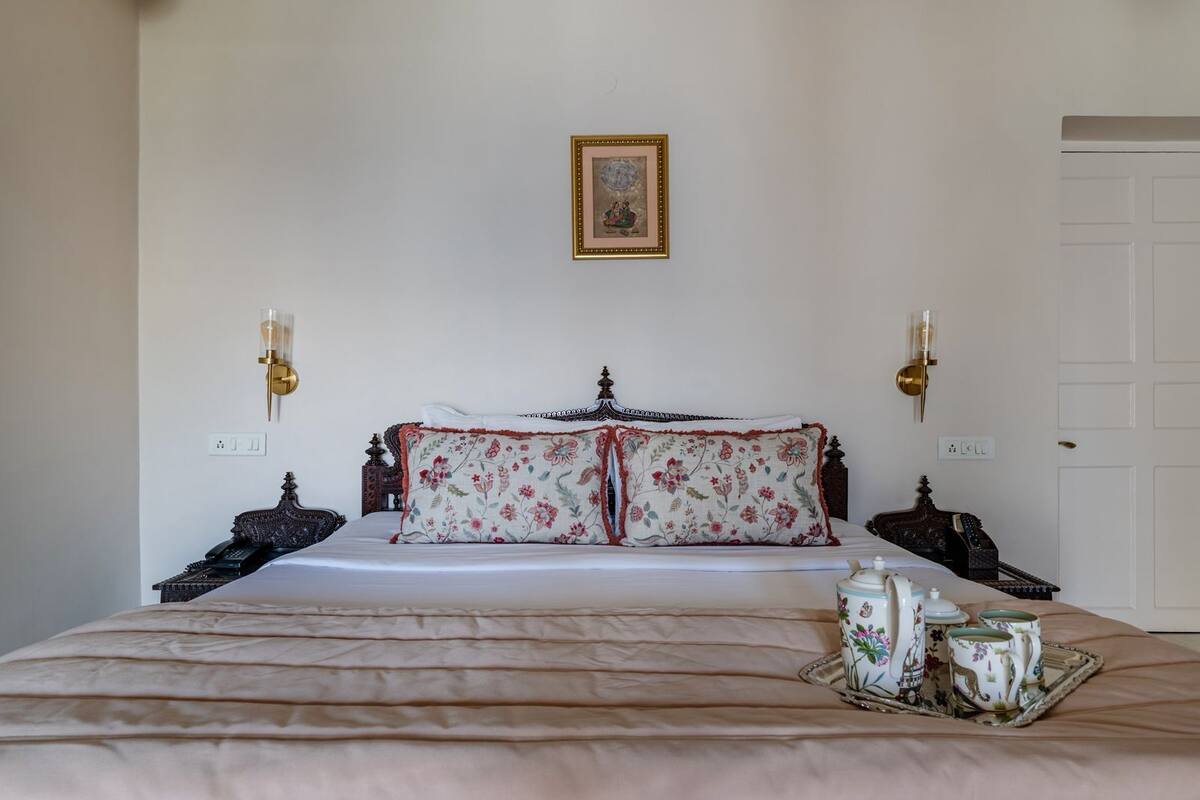 A neatly made bed with floral bedding, a bedside table with a lamp, and a tray with teacups.
