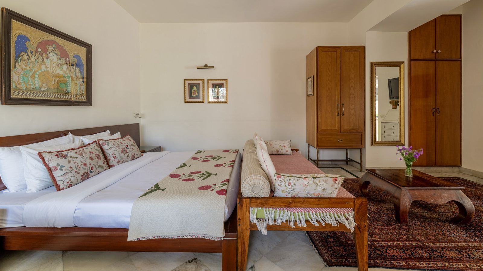 A bedroom with a bed, a wooden nightstand, a wooden chair, a wooden wardrobe, and a mirror.