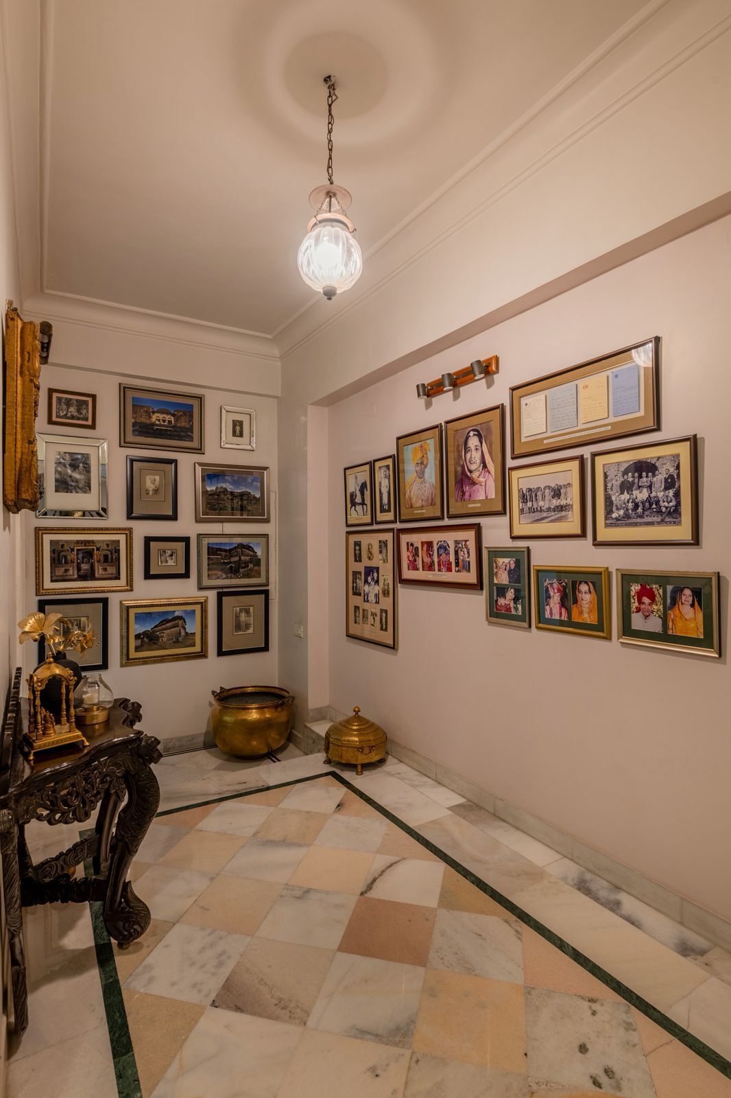 Una habitación con piso de baldosas, un candelabro, cuadros enmarcados en las paredes y una mesa decorativa con un florero.