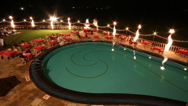 A swimming pool with a spiral design, surrounded by red tables and chairs, and string lights. - Nazri Resort (Baga)