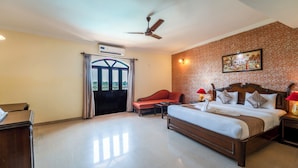 A hotel room with a bed, a desk, a chair, a ceiling fan, and a window with curtains. - Nazri Resort (Baga)