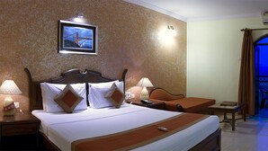 A hotel room with a bed, bedside tables, a desk, a chair, and a view of a cityscape through a large window. - Nazri Resort (Baga)
