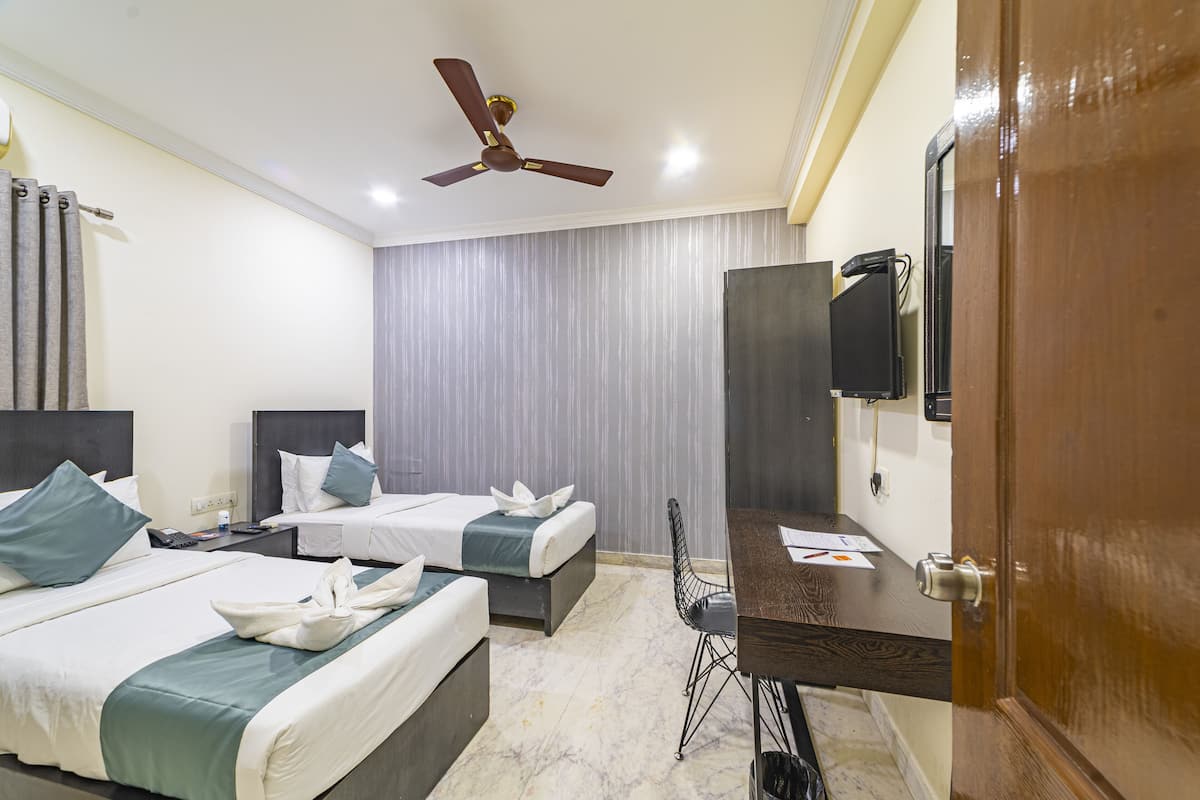 Habitación de hotel con dos camas, un escritorio, una silla, un ventilador de techo y un televisor montado en la pared.