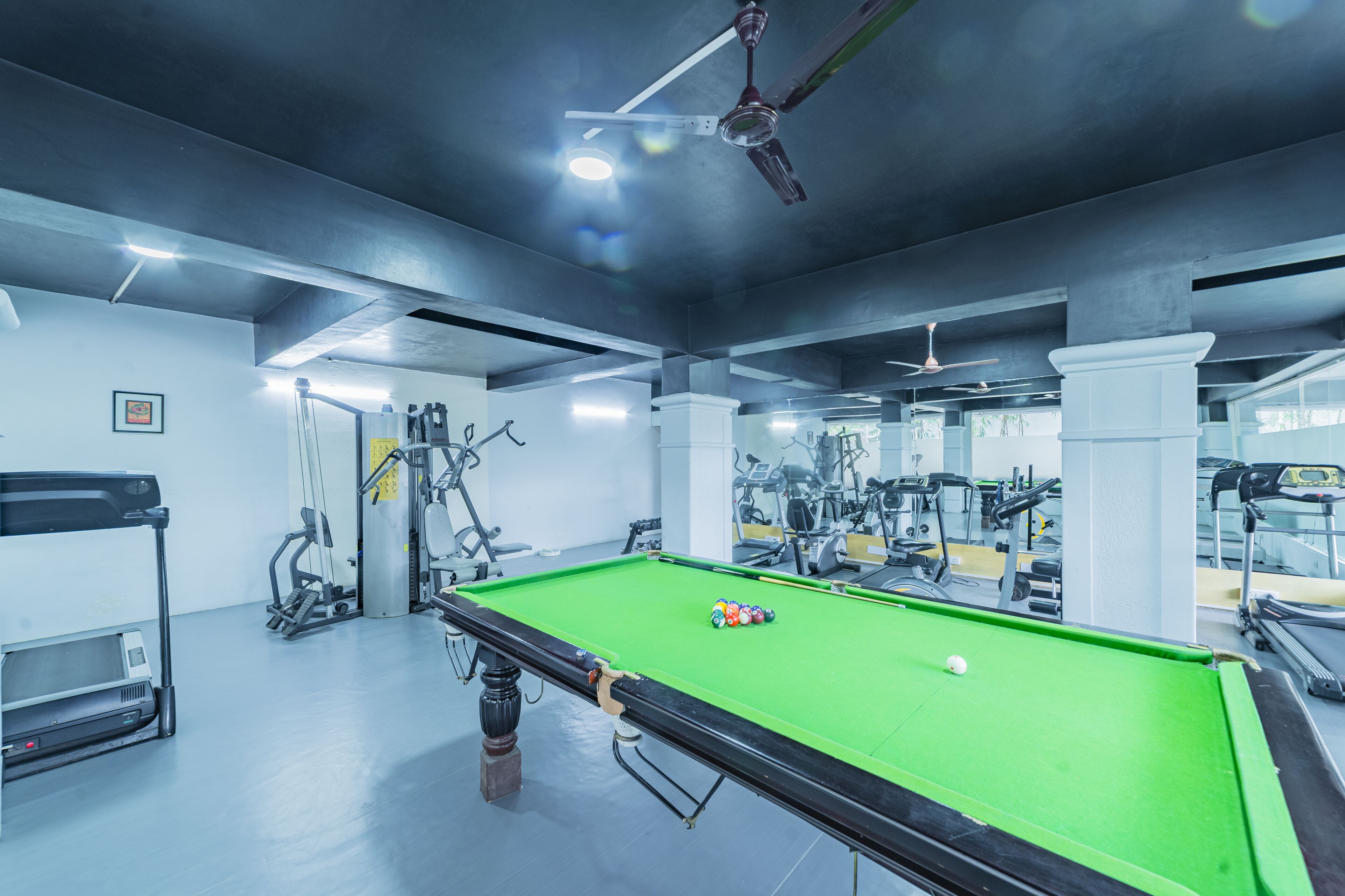 A pool table in a gym with exercise equipment around.