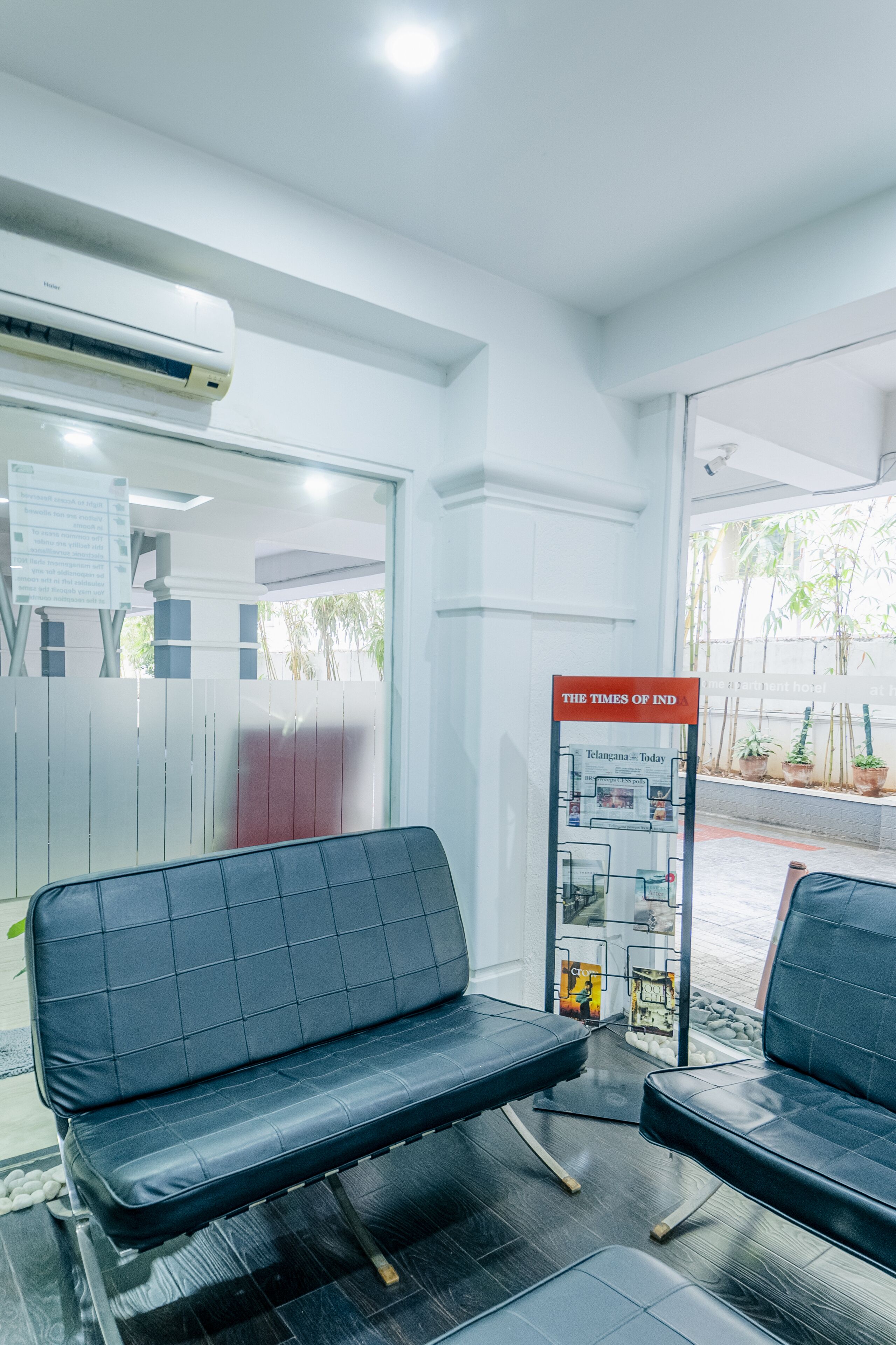 A waiting area with a bench, a newspaper stand, and an air conditioning unit.