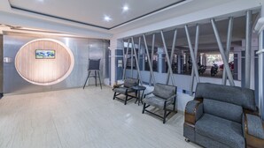 A modern lobby with a circular wooden wall, grey seating, and a large TV screen. - Hotel Athome & Serviced Apartments by Deccan Serai Hotels (Hyderabad)