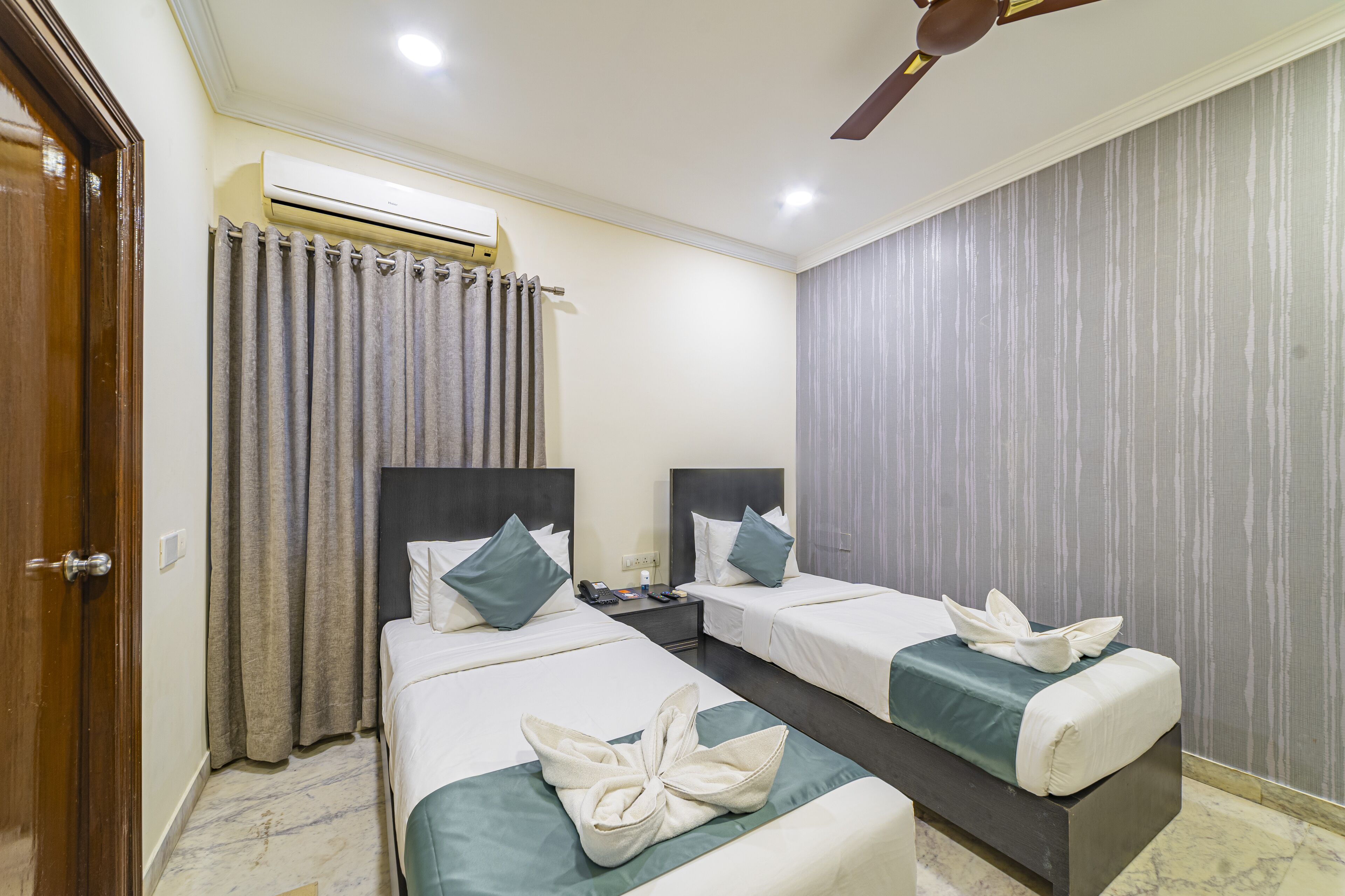 A hotel room with two beds, a wooden door, an air conditioning unit, a ceiling fan, and a curtain.