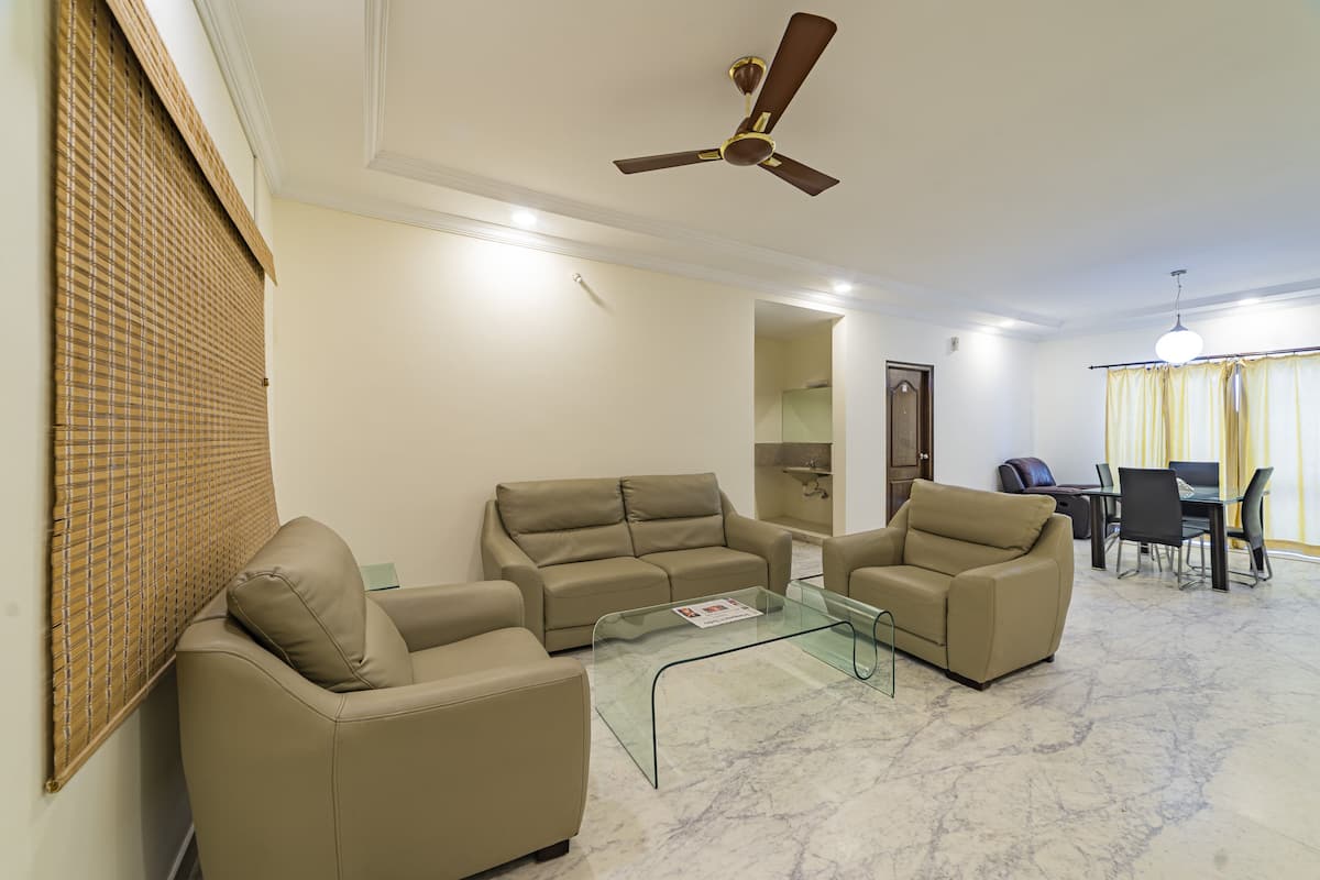 Una sala de estar con sofás color beige, una mesa de centro de vidrio y un ventilador de techo.