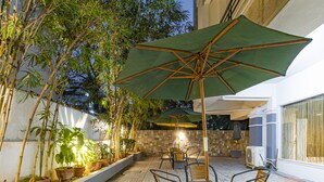 An outdoor patio with a brick floor, potted plants, and a table with chairs under a large umbrella. - Hotel Athome & Serviced Apartments by Deccan Serai Hotels (Hyderabad)