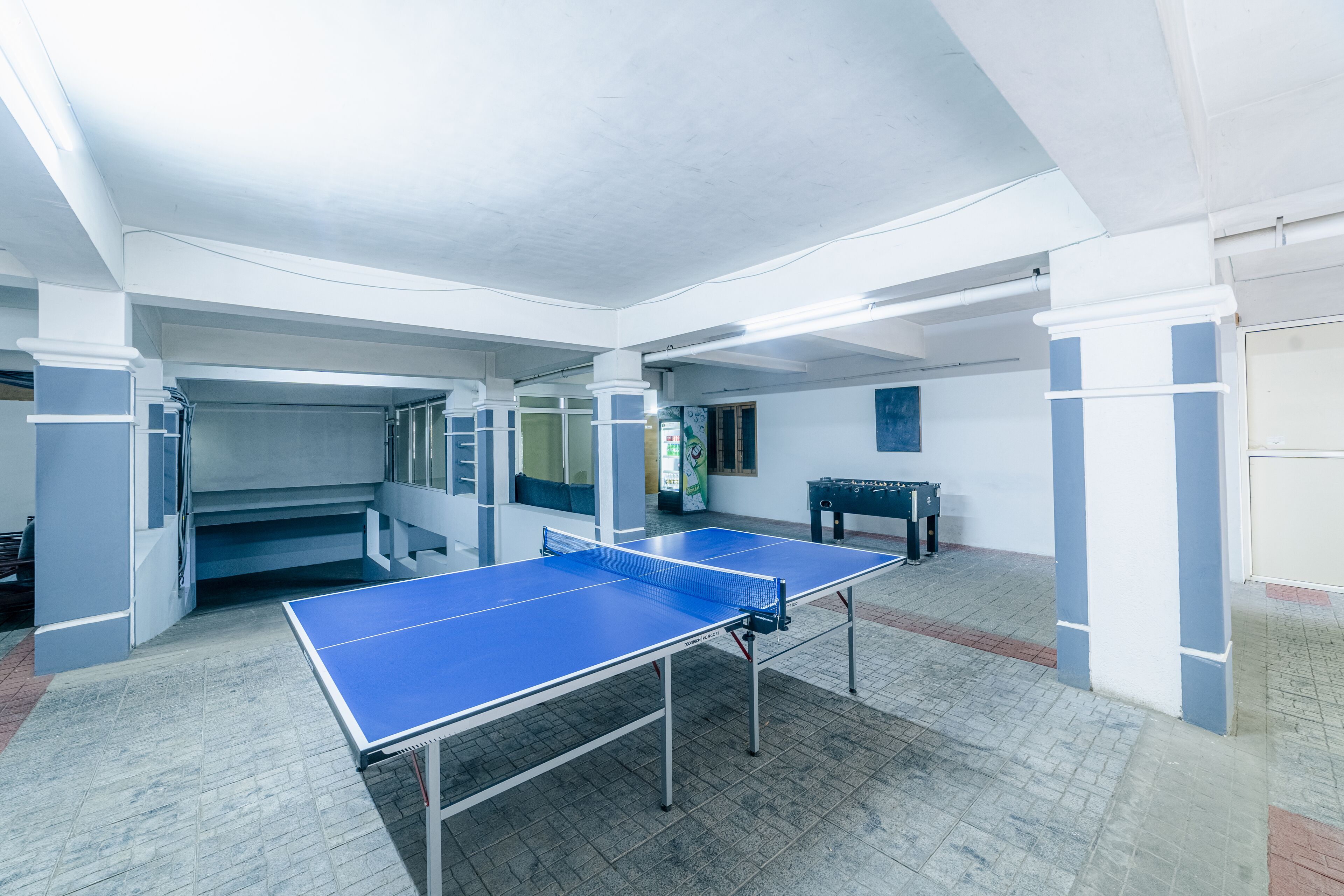 A spacious indoor area with a ping pong table, a bench, and a small table with a drink dispenser.