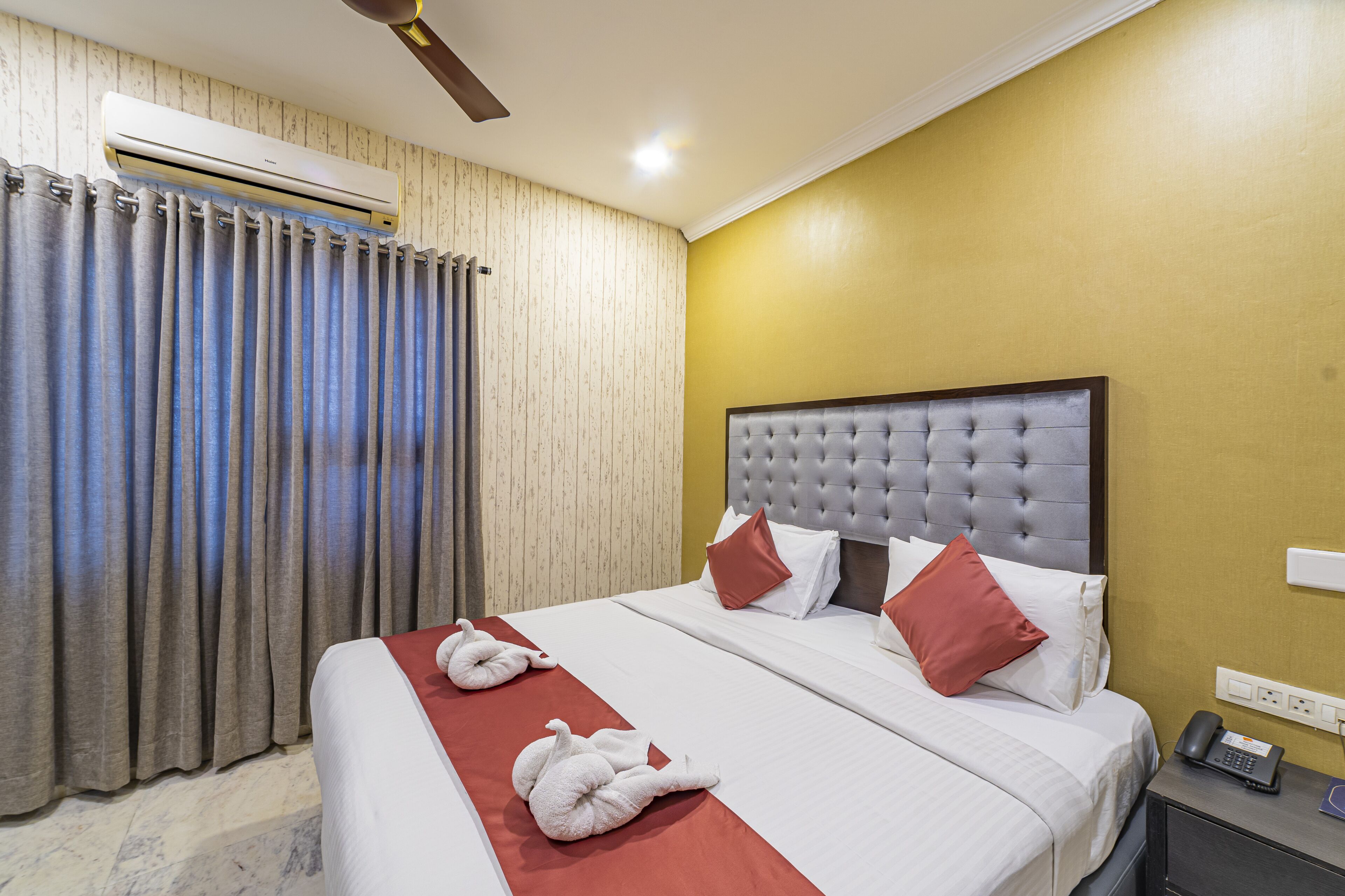 A hotel room with a large bed, a ceiling fan, an air conditioning unit, and a telephone on a bedside table.