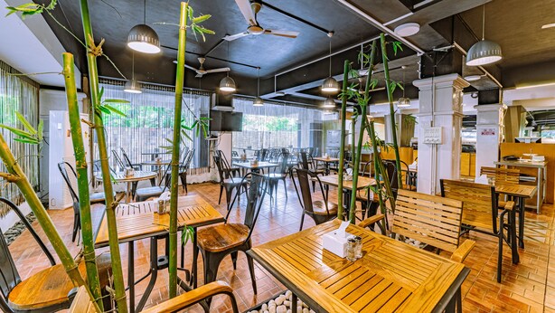A restaurant with bamboo plants, wooden tables, and black chairs. - Hotel Athome & Serviced Apartments by Deccan Serai Hotels (Hyderabad)