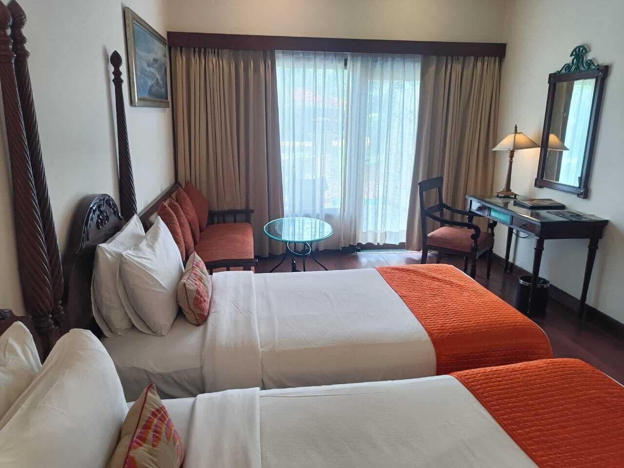 A hotel room with two beds, a desk, a chair, a small table, and a window with curtains.