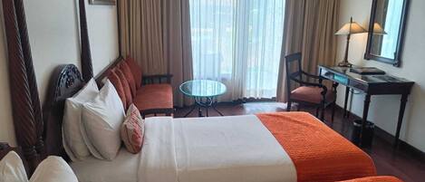 A hotel room with two beds, a desk, a chair, a small table, and a window with curtains.
