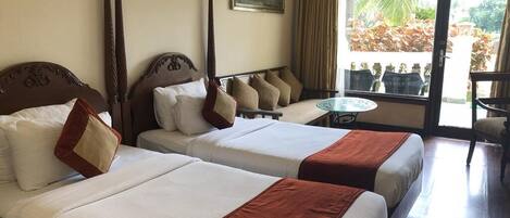 A hotel room with two beds, a balcony with a table, and a view of the outdoors.