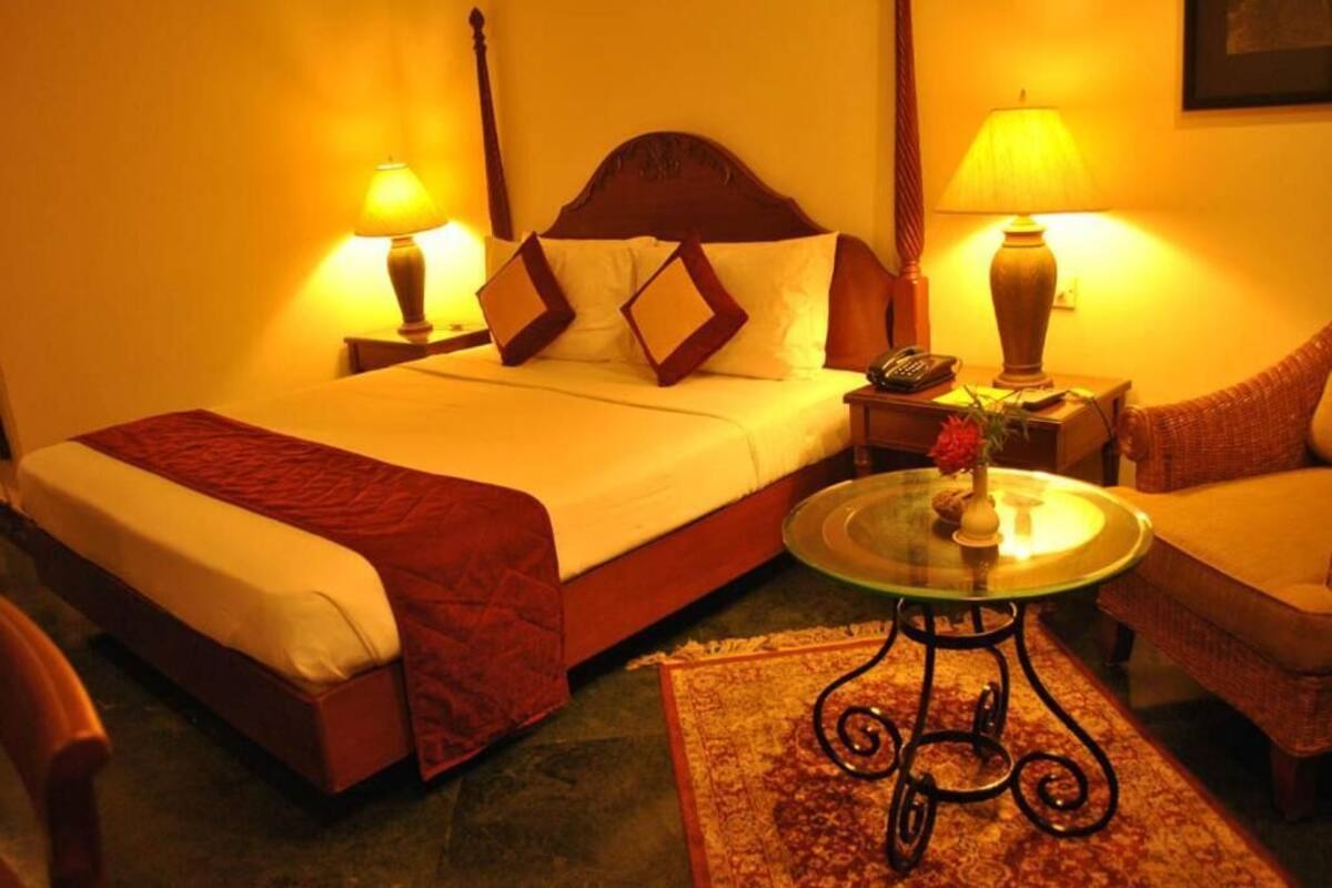 Une chambre d’hôtel comprenant un lit, deux tables de chevet avec des lampes, une petite table ronde avec un vase et une chaise.