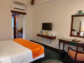 Una habitación de hotel con cama, escritorio, silla, televisor, espejo y aire acondicionado.