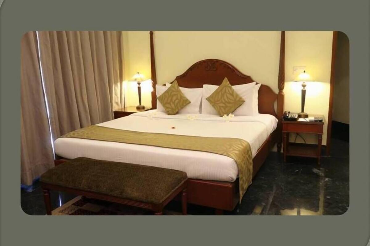 Une chambre d’hôtel avec un grand lit, deux tables de chevet, un banc et des rideaux.