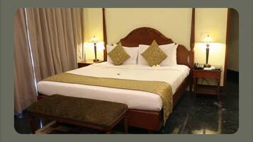 Una habitación de hotel con una cama grande, dos mesitas de noche, un banco y cortinas.