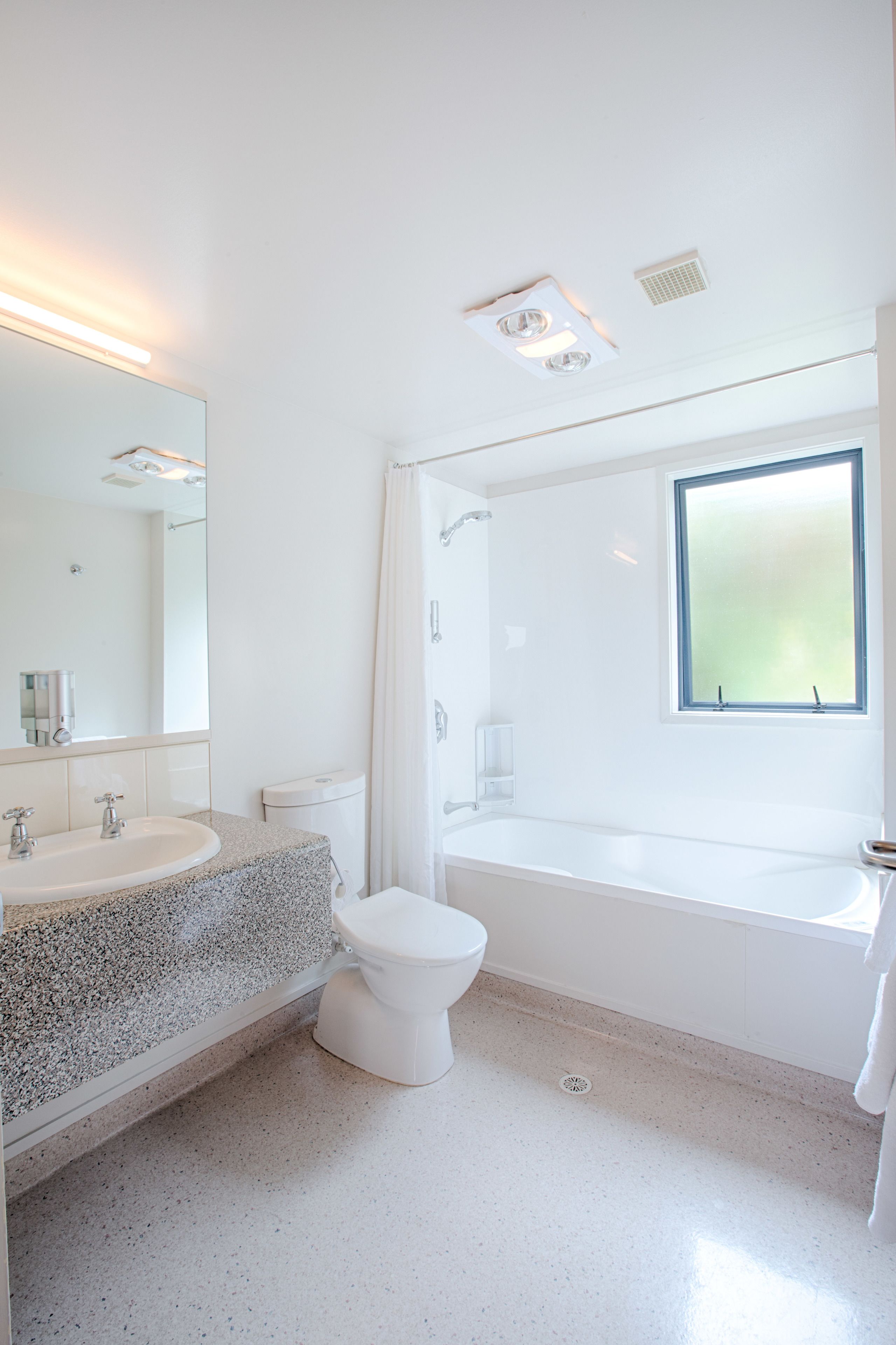 A modern bathroom with a white sink, toilet, and bathtub, a large mirror, and a window.